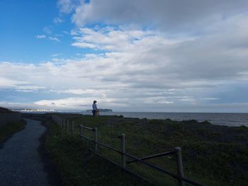 Man standing on railing by sea against sky