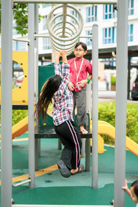 Young asian children hang on the monkey bar. to exercise at outdoor playground in the neighbourhood.