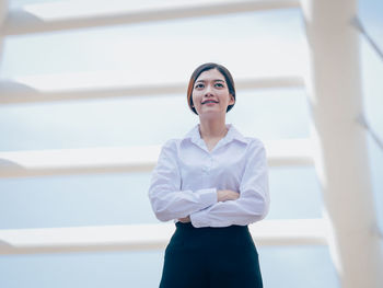 Smiling young woman with arms crossed standing against building