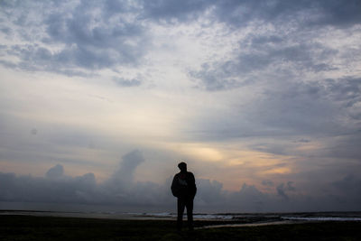 Rear view of man standing on land against sky during sunset