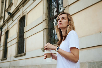 Young woman looking down while standing against brick wall