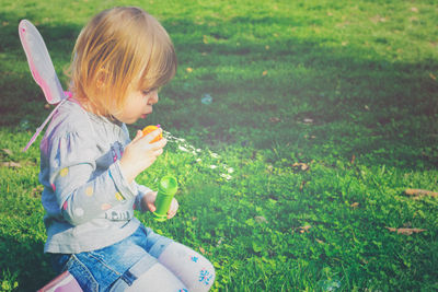 Side view of cute girl blowing bubbles while sitting in park