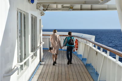 Rear view of mother and son walking on boat deck