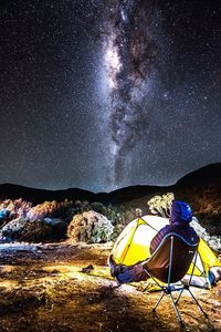 Person sitting by tent against star field at night