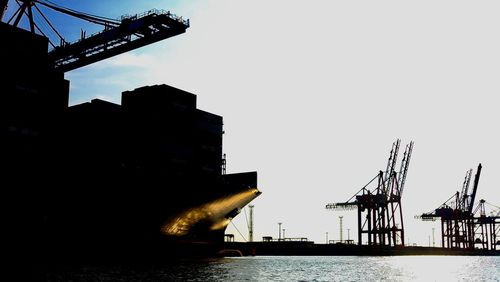 Silhouette cranes at commercial dock against clear sky