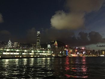 Illuminated buildings by river against sky at night