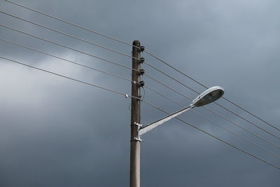 Low angle view of electricity pylon against stormy clouds