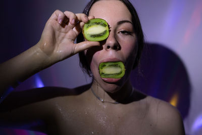 Portrait of woman with kiwi fruit against wall