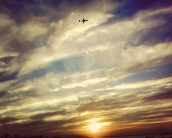 Low angle view of airplane flying against cloudy sky