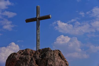 Low angle view of cross on rock against sky