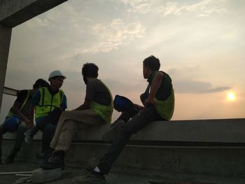 People sitting by sea against sky during sunset