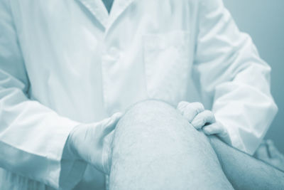 Midsection of doctor examining patient knee in hospital