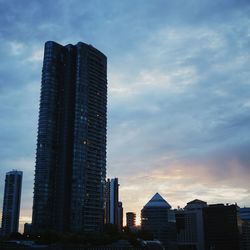 Low angle view of skyscrapers against cloudy sky