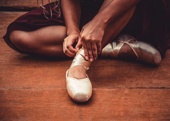 Low section of woman fastening ballet shoe on hardwood floor