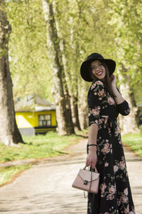 Portrait of smiling woman wearing hat standing against trees