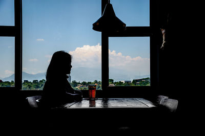 Silhouette woman having drink while sitting by window at restaurant