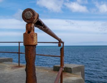 Metal railing on beach against sky