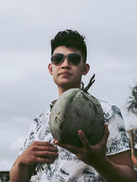 Portrait of young man holding coconut against sky