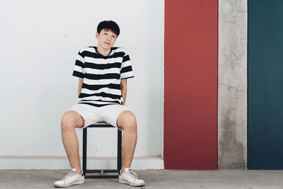 Full length of young man sitting against wall