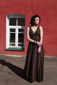 Beautiful woman in brown dress standing against red wall