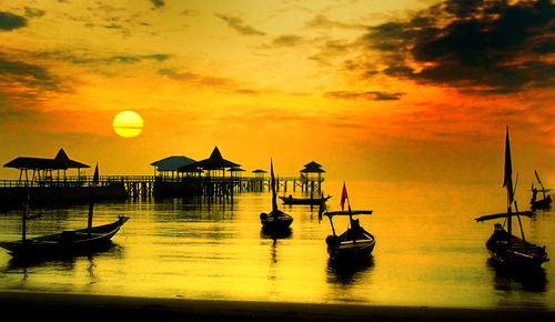 Silhouette boats in sea against orange sky