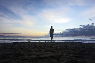 Rear view of silhouette man standing on beach against sky