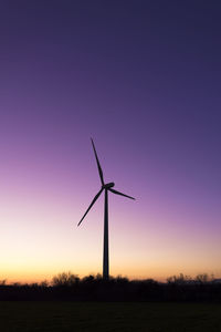 Wind turbines on field against clear sky during sunset
