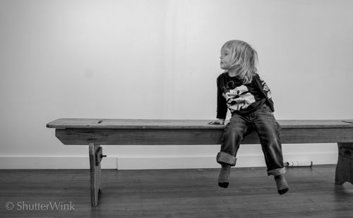Full length of girl looking away while sitting on bench at home