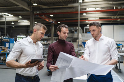 Male professionals discussing over blueprint at factory