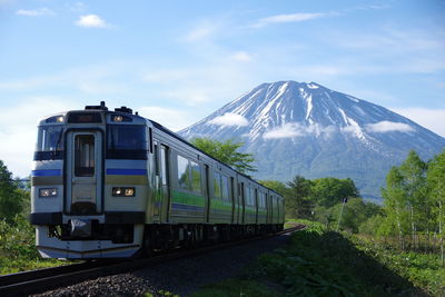 Train on railroad track by mt yotei against sky