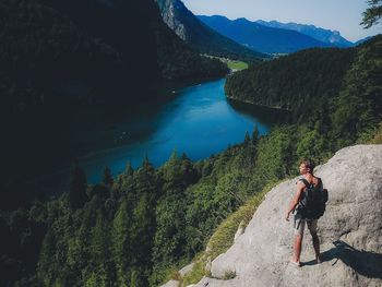 Man standing on cliff by lake against sky