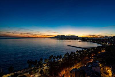 High angle view of illuminated city by sea against sky