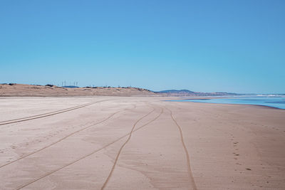 Tyre track and footprints mark on sand with seascape and blue sky