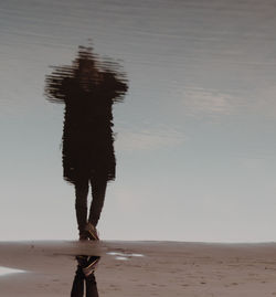 Low section of man standing on beach against sky