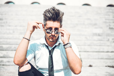 Portrait of young man holding eyeglasses standing outdoors