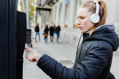 Young woman listening to music using parking meter