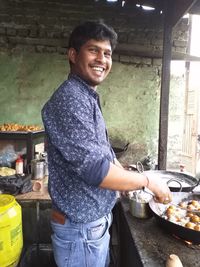 Smiling young man holding food while standing in kitchen