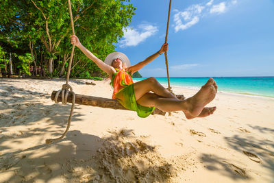 Woman swinging on beach by sea against sky