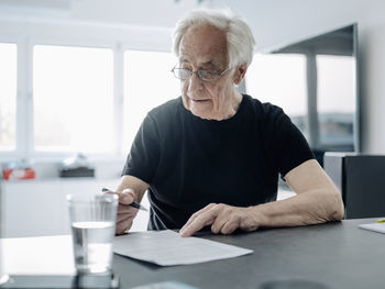 Businessman wearing eyeglasses writing in paper while sitting at office