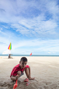 Portrait of boy crouching at beach against sky