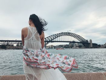 Rear view of woman standing against arch bridge over river