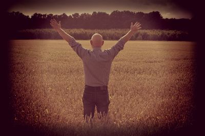 Rear view of man with arms outstretched standing on field