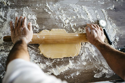 Cropped hands of man rolling dough on table in kitchen