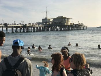 People on pier at beach against sky