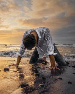 Man working at beach against sky during sunset