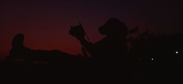 Silhouette man and woman standing against sky at night