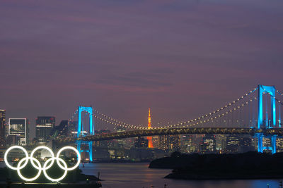 Illuminated bridge over river with city in background