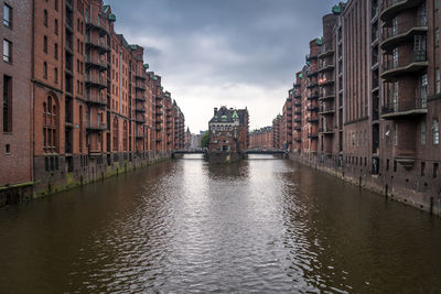 Canal amidst buildings in city against sky