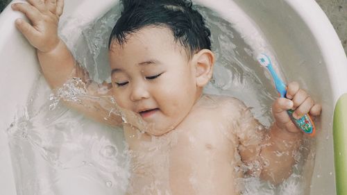 High angle view of shirtless baby boy lying in bathtub