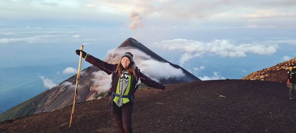 Happy woman standing on top of a vulcano with an active vulcano in the backround